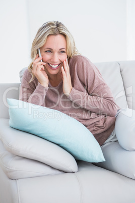 Smiling blonde sitting on couch phoning Smiling blonde sitting on couch phoning
