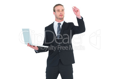 Serious businessman writing with marker and holding laptop