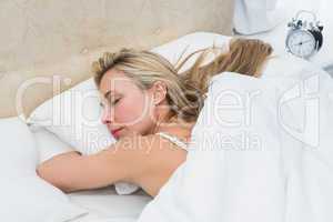 Pretty blonde sleeping in bed with alarm clock