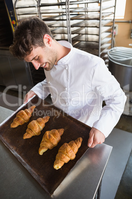 Baker showing some croissants on a baking tray