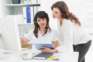 Smiling coworkers using computer and tablet pc