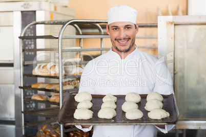 Smiling baker holding tray of raw dough