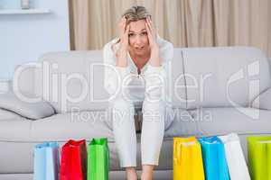 Blonde sitting on couch getting headache near shopping bags
