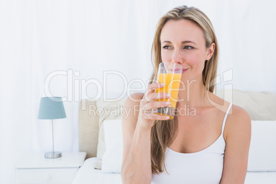 Smiling blonde drinking glass of orange juice