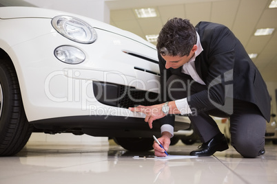 Man looking at the bumper while writing on clipboard