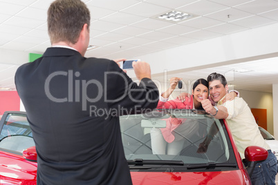 Businessman taking picture of the couple in their new car