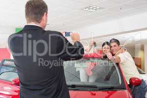 Businessman taking picture of the couple in their new car