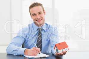 Businessman taking notes and showing miniature house