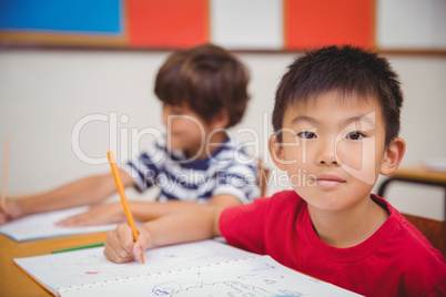 Cute pupils drawing at their desks one smiling at camera