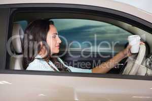 Smiling woman driving car while drinking coffee