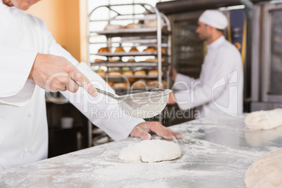 Baker sieving flour on the dough