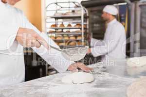 Baker sieving flour on the dough