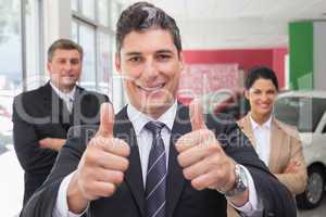 Smiling business team standing while one giving thumbs up