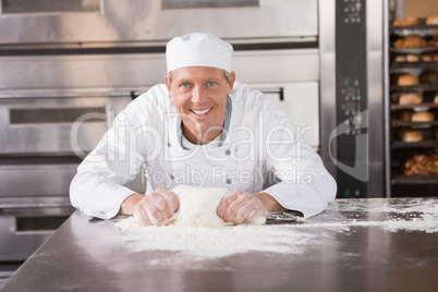 Smiling baker kneading dough on counter