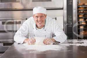 Smiling baker kneading dough on counter
