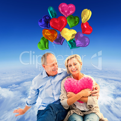 Composite image of happy mature couple with heart pillow