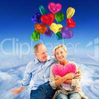 Composite image of happy mature couple with heart pillow