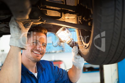 Mechanic shining torch under car