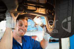 Mechanic shining torch under car