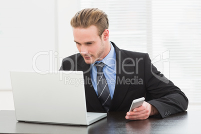 Classy businessman using laptop and mobile phone