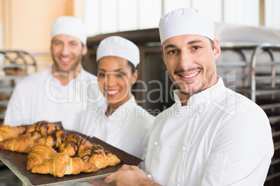 Team of bakers smiling at camera with trays of croissants
