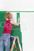 Frau auf Leiter streicht Wand gruen