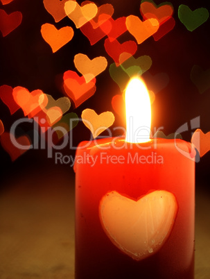 Red candle on the table and shiny hearts in background.