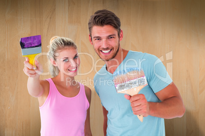 Composite image of young couple smiling and holding paintbrushes