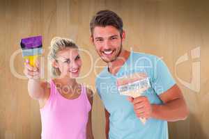 Composite image of young couple smiling and holding paintbrushes