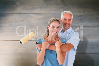 Composite image of happy couple hugging and holding paint roller