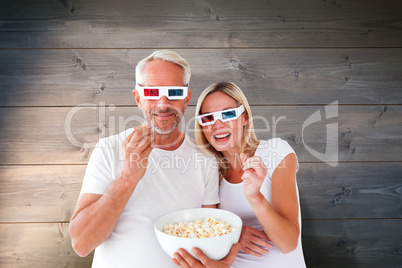 Composite image of happy couple wearing 3d glasses eating popcor