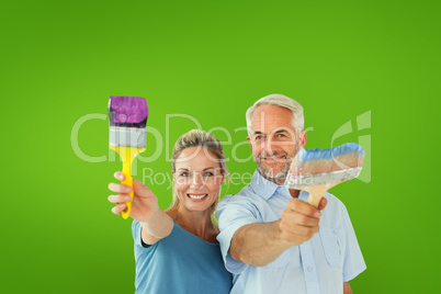 Composite image of happy couple holding paintbrushes smiling at