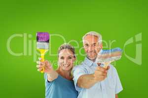 Composite image of happy couple holding paintbrushes smiling at