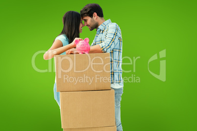 Composite image of happy young couple with moving boxes and pigg