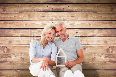 Composite image of happy couple sitting and holding house outlin