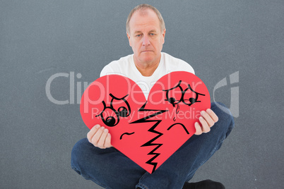 Composite image of upset man sitting holding heart shape