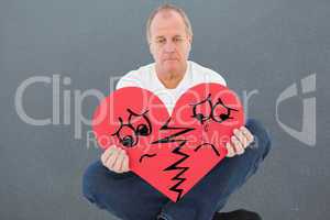 Composite image of upset man sitting holding heart shape