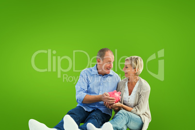 Composite image of happy mature couple holding piggy bank