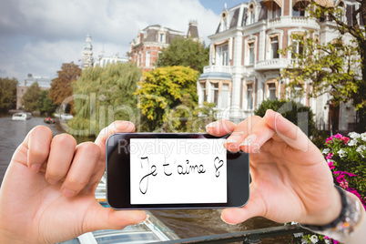 Composite image of hand holding smartphone showing je taime