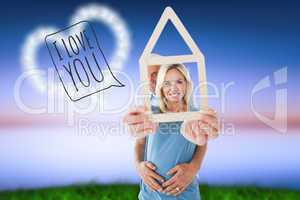 Composite image of happy couple holding house outline