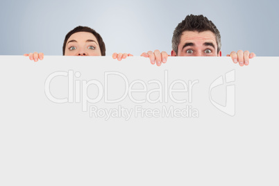 Composite image of man and woman hiding behind a white board wit