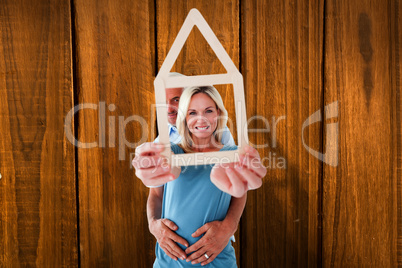 Composite image of happy couple holding house outline