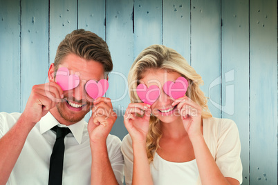 Composite image of attractive young couple holding pink hearts o