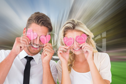 Composite image of attractive young couple holding pink hearts o