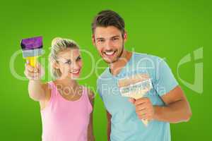 Composite image of young couple smiling and holding paintbrushes