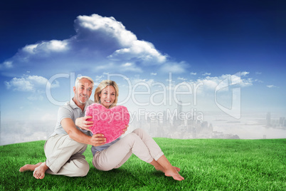 Composite image of happy couple sitting and holding heart pillow