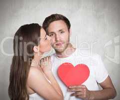 Composite image of woman kissing man as he holds heart
