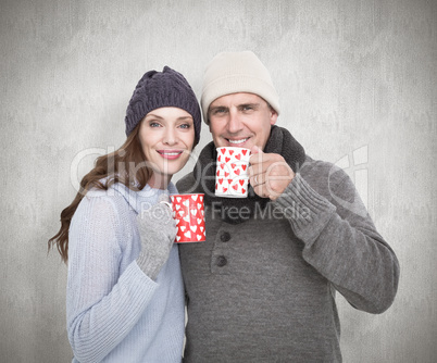 Composite image of happy couple in warm clothing holding mugs