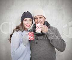 Composite image of happy couple in warm clothing holding mugs