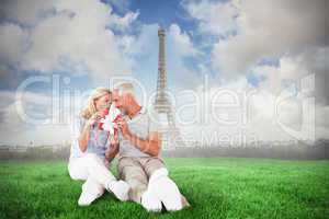 Composite image of happy couple sitting and holding present